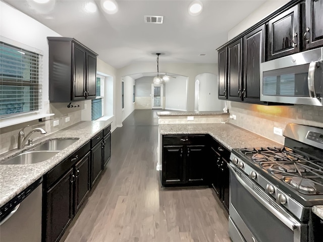 kitchen with light stone counters, stainless steel appliances, sink, pendant lighting, and light hardwood / wood-style flooring