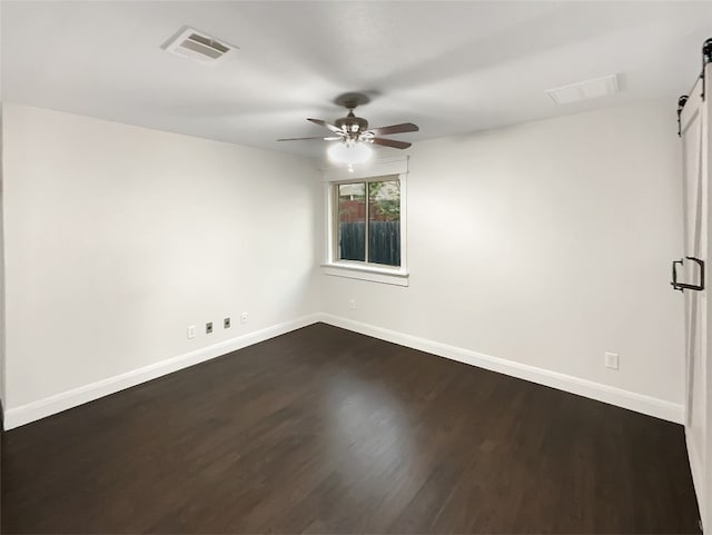 unfurnished room with ceiling fan, a barn door, and dark hardwood / wood-style floors