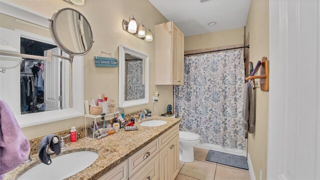 bathroom featuring tile patterned flooring, double vanity, toilet, and a sink