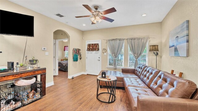 living room featuring visible vents, ceiling fan, baseboards, wood finished floors, and arched walkways