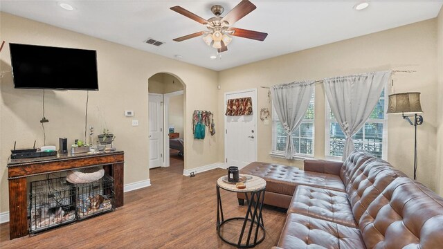 living area featuring visible vents, a ceiling fan, wood finished floors, arched walkways, and baseboards