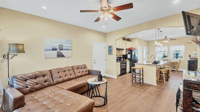 living room featuring recessed lighting, arched walkways, light wood-style floors, baseboards, and ceiling fan