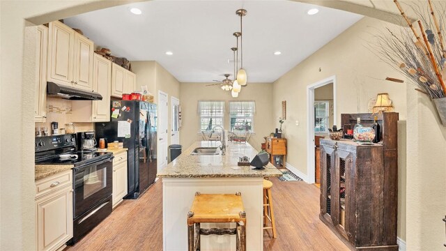 kitchen featuring a sink, black appliances, under cabinet range hood, cream cabinets, and light wood-type flooring