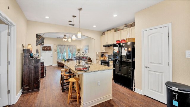 kitchen featuring dark wood finished floors, black appliances, a kitchen bar, and ceiling fan