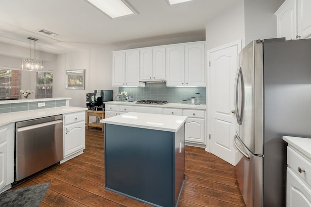 kitchen featuring appliances with stainless steel finishes, dark wood-type flooring, pendant lighting, white cabinets, and a center island