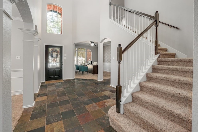 entryway with a towering ceiling, ornate columns, ceiling fan, and a healthy amount of sunlight