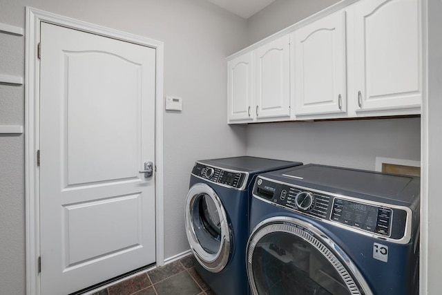 laundry room with washing machine and clothes dryer, dark tile patterned floors, and cabinets