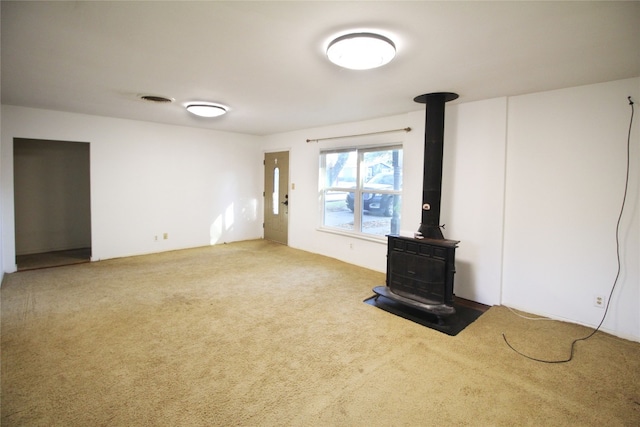 unfurnished living room featuring a wood stove and carpet flooring