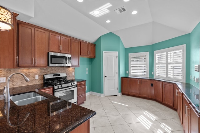 kitchen featuring decorative backsplash, stainless steel appliances, sink, dark stone counters, and vaulted ceiling