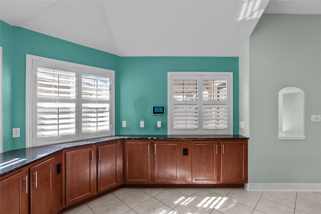 interior space with dark stone countertops, lofted ceiling, a healthy amount of sunlight, and light tile patterned floors