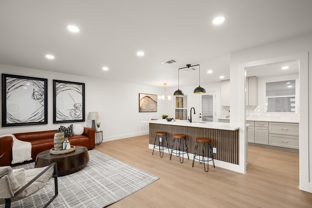 kitchen with decorative backsplash, a center island with sink, light hardwood / wood-style flooring, and hanging light fixtures