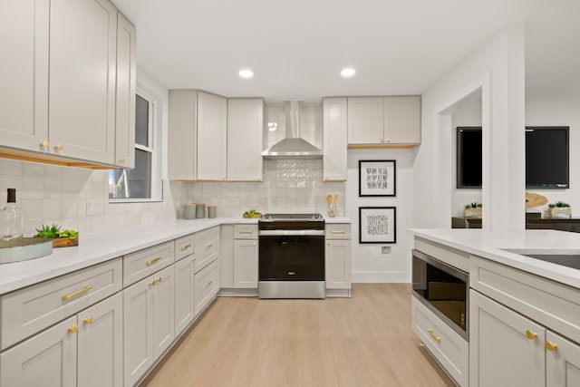 kitchen with wall chimney range hood, decorative backsplash, light hardwood / wood-style floors, white cabinetry, and stainless steel appliances