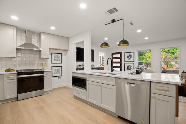 kitchen with pendant lighting, sink, wall chimney exhaust hood, light hardwood / wood-style floors, and stainless steel appliances