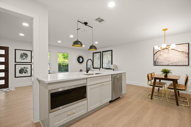 kitchen featuring stainless steel appliances, light hardwood / wood-style flooring, hanging light fixtures, and sink