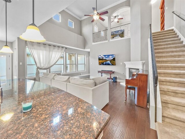 living room featuring a high ceiling, dark hardwood / wood-style flooring, crown molding, and ceiling fan