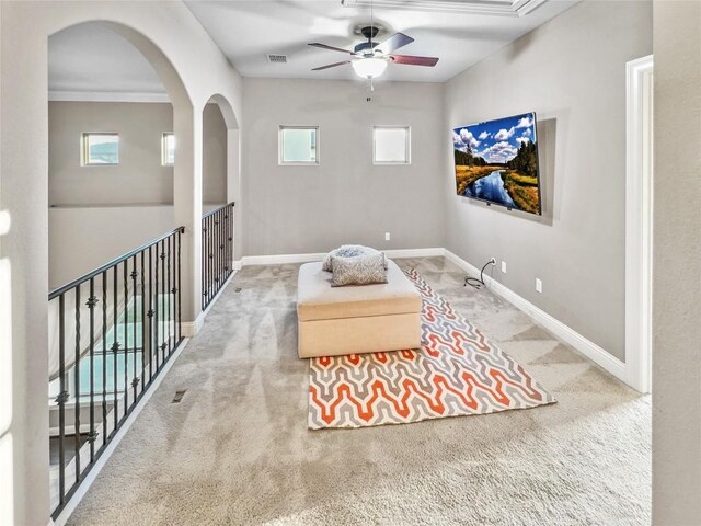 living area with ornamental molding, carpet flooring, and ceiling fan