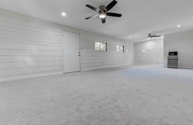 unfurnished living room featuring light carpet, wooden walls, and ceiling fan