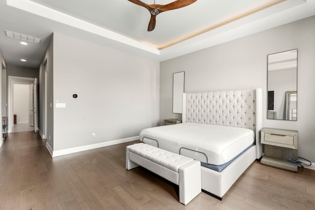 bedroom with hardwood / wood-style floors, ceiling fan, and a tray ceiling