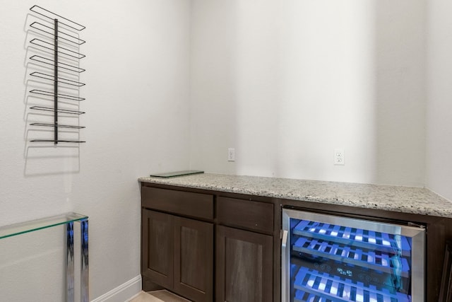 bar featuring dark brown cabinetry, wine cooler, and light stone counters