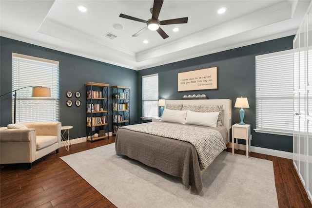 bedroom with ceiling fan, a raised ceiling, crown molding, and dark hardwood / wood-style flooring