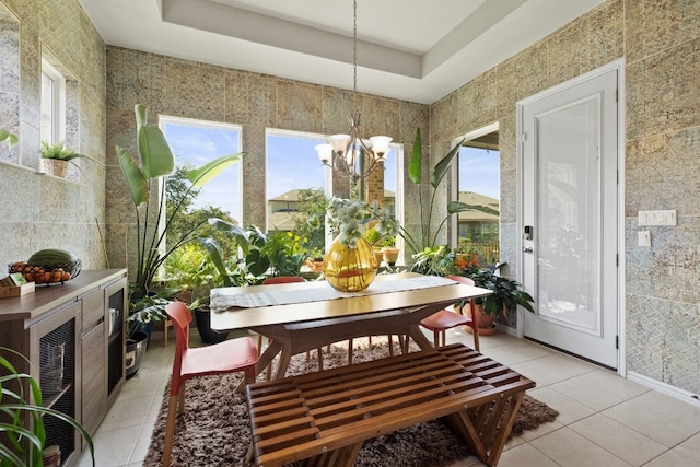 sunroom / solarium with a healthy amount of sunlight, a raised ceiling, and an inviting chandelier