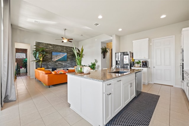 kitchen with ceiling fan, stainless steel appliances, light stone counters, an island with sink, and white cabinets