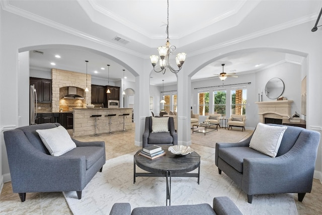 living room with ceiling fan with notable chandelier, ornamental molding, light tile patterned flooring, and a raised ceiling