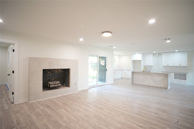 unfurnished living room with a tile fireplace, light hardwood / wood-style flooring, and sink