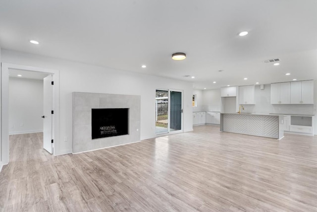 unfurnished living room with a tile fireplace, recessed lighting, a sink, visible vents, and light wood finished floors