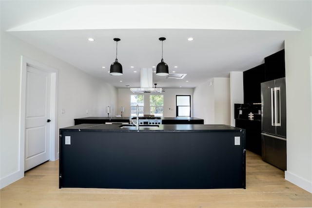 kitchen with island exhaust hood, high end refrigerator, light hardwood / wood-style floors, and a kitchen island with sink