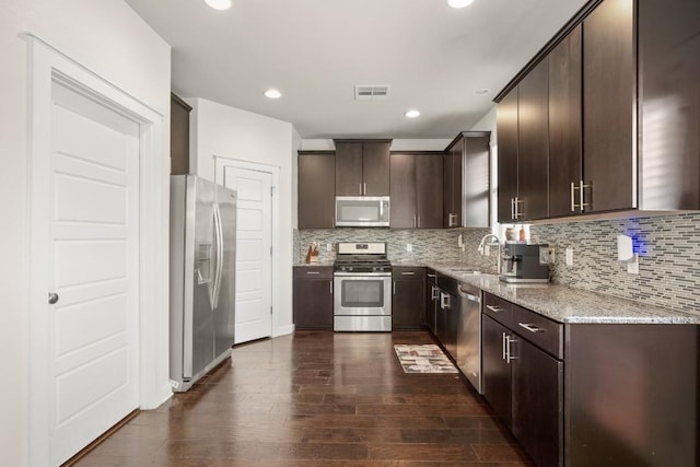 kitchen with stainless steel appliances, light stone counters, dark hardwood / wood-style flooring, decorative backsplash, and dark brown cabinets