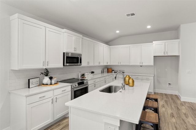 kitchen with white cabinets, sink, a kitchen island with sink, appliances with stainless steel finishes, and a kitchen breakfast bar