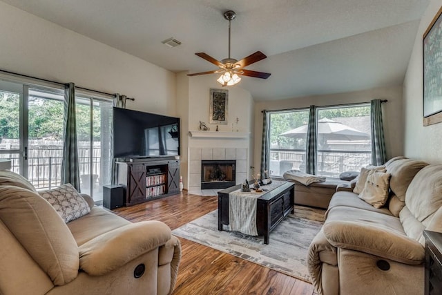 living room with a tile fireplace, ceiling fan, vaulted ceiling, and hardwood / wood-style flooring