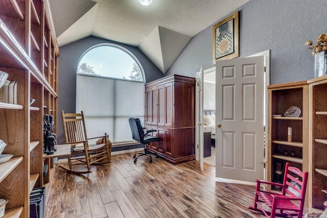office area with a textured ceiling, wood-type flooring, and vaulted ceiling