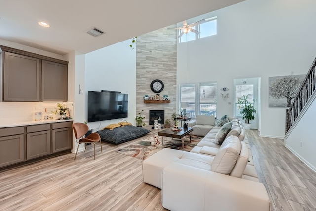 living room featuring a fireplace, a towering ceiling, light wood-type flooring, and ceiling fan