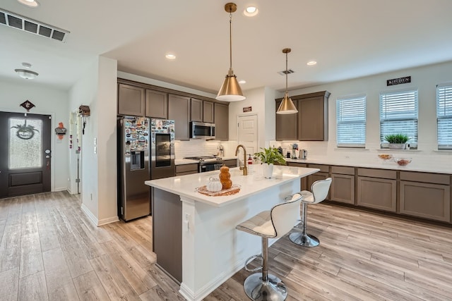 kitchen featuring light hardwood / wood-style floors, pendant lighting, a center island with sink, appliances with stainless steel finishes, and a kitchen bar