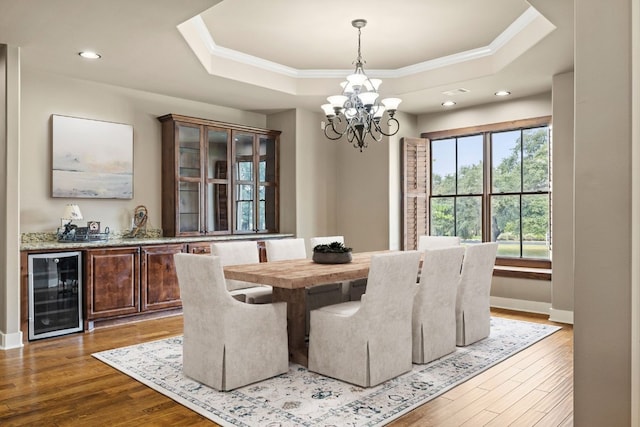 dining area featuring a tray ceiling, wood finished floors, beverage cooler, and ornamental molding