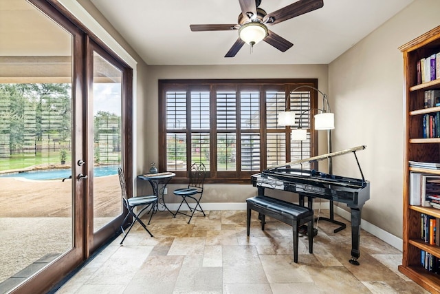 sitting room with stone finish floor, a ceiling fan, and baseboards