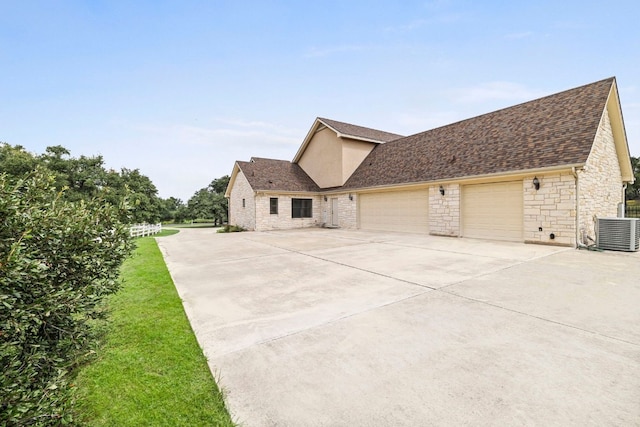 view of side of property featuring central air condition unit, stone siding, concrete driveway, a shingled roof, and a garage