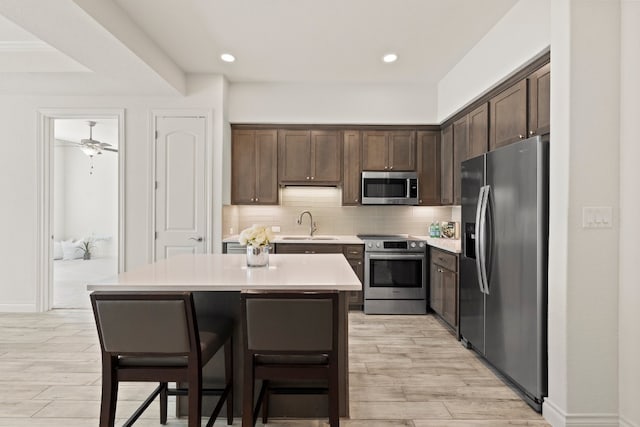 kitchen featuring light wood-type flooring, tasteful backsplash, sink, appliances with stainless steel finishes, and a center island