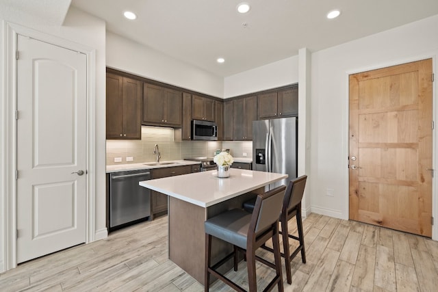 kitchen with dark brown cabinetry, appliances with stainless steel finishes, a kitchen breakfast bar, a center island, and light hardwood / wood-style floors