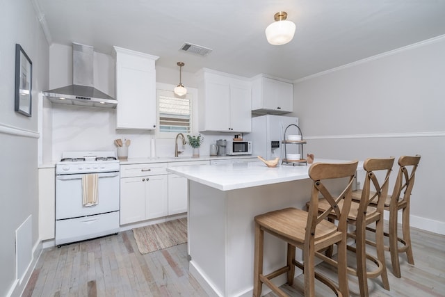 kitchen with white appliances, wall chimney range hood, light hardwood / wood-style floors, and white cabinets