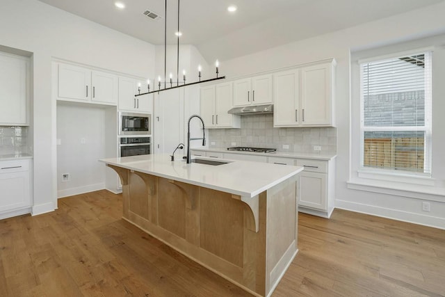 kitchen featuring pendant lighting, white cabinetry, an island with sink, sink, and black appliances