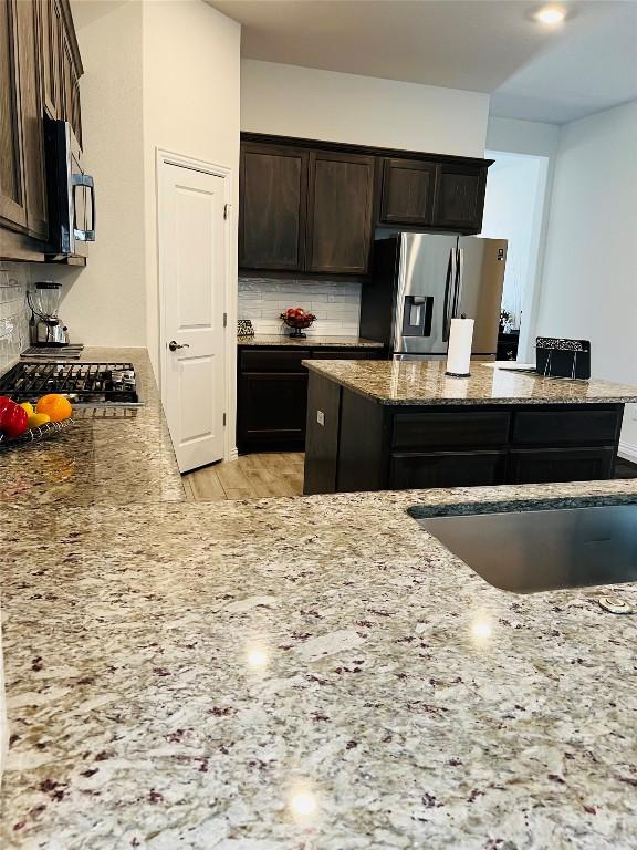 kitchen with stone counters, appliances with stainless steel finishes, decorative backsplash, and dark brown cabinets