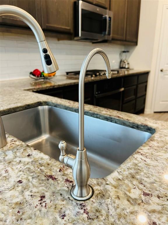 details featuring backsplash, dark brown cabinets, light stone countertops, and sink