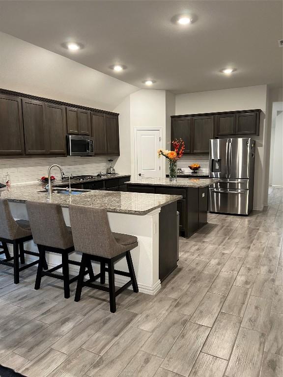 kitchen with a breakfast bar, appliances with stainless steel finishes, a center island with sink, and light stone counters