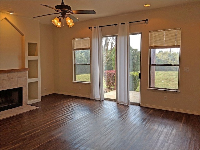 unfurnished living room with ceiling fan, built in features, dark wood-type flooring, and a healthy amount of sunlight