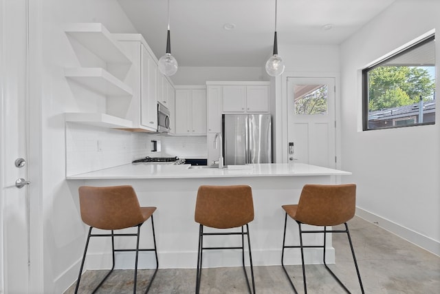 kitchen with kitchen peninsula, white cabinets, tasteful backsplash, a breakfast bar area, and appliances with stainless steel finishes