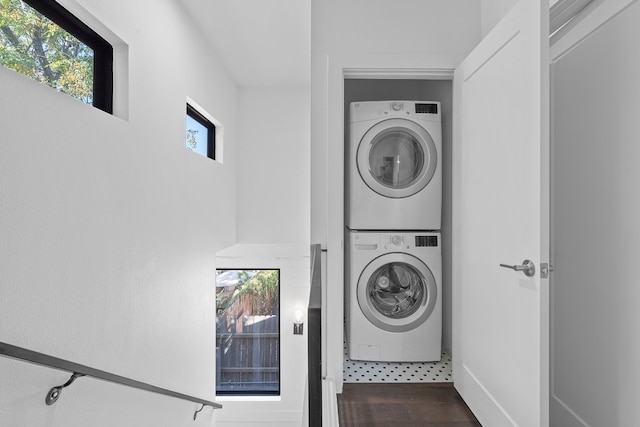 clothes washing area with dark wood-type flooring, a healthy amount of sunlight, and stacked washer and clothes dryer