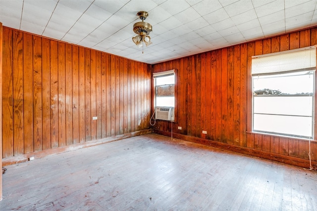 empty room featuring light wood-type flooring, wooden walls, ceiling fan, and cooling unit